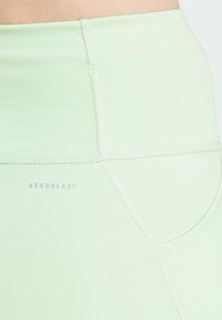 Leggings sportivi verde chiaro realizzati in tessuto morbido, con vita piatta, cuciture visibili e un'etichetta "AEROREADY".