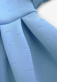 Svetloblúzka šaty s jemnou, štruktúrovanou tkaninou a embosovanými vzormi písmena "B" a motýlikmi. Dizajn obsahuje záhyby pre pridanie detailu.