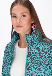 Jachetă puffer teal cu un imprimeu leopard alb-negru și roz, guler înalt și fermoar în față. Asortată cu cercei mari în formă de stea roz.