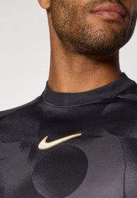 Černé sportovní tričko s elegantním designem, kulatým výstřihem a zlatým logem Nike na hrudi. Hladká textura s jemnými vzory.