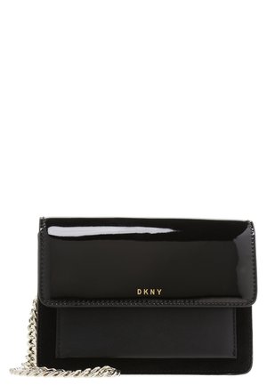 Czarna skórzana torebka DKNY na ramię z błyszczącą klapką, złotym logo i srebrnym łańcuszkowym paskiem na białym tle.
