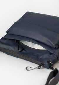 Borsa impermeabile in colore navy con chiusura a zip, interni rivestiti in peluche e una tracolla regolabile. Presenta una texture liscia e un design minimale.