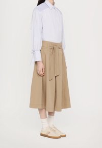 Raitoitettu sininen ja valkoinen napitettava paita pitkillä hihoilla, yhdistettynä beigeen korkeavyötäröiseen kietaisuhameeseen, valkoisiin sukkiin ja vaaleisiin kenkiin.