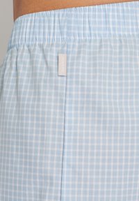 Tissu à carreaux bleu clair avec une taille élastique, une couture latérale et une étiquette affichant "HANRO". Texture douce et design léger.