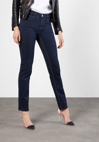 Jeans de mezclilla azul oscuro con un ajuste slim, que cuentan con costuras de contraste claras y diseño de cinco bolsillos, combinados con tacones de dos tonos.