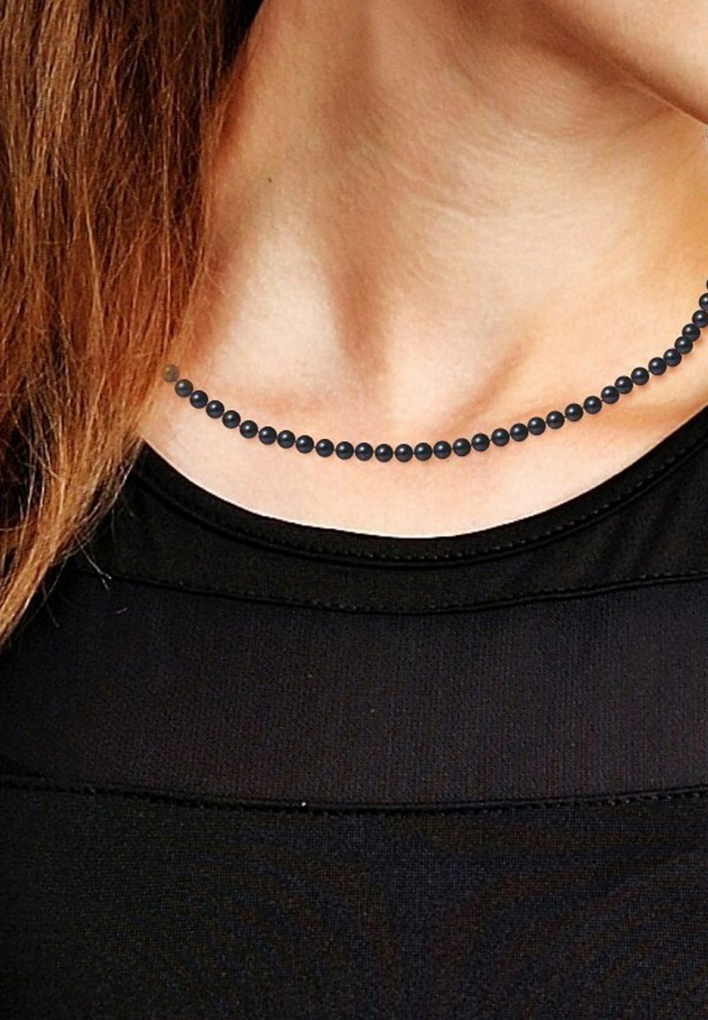 Collier de perles noires avec une texture lisse et uniforme, composé de perles sphériques espacées régulièrement. Porté au-dessus d'un haut noir sur un cou dénudé.