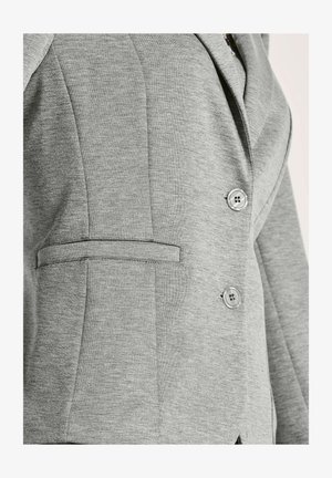 Nahaufnahme eines grauen Blazers mit zwei Knöpfen und einer horizontalen Leistentasche auf der linken Seite.