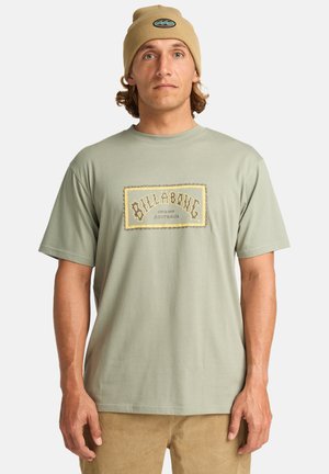 Light green cotton T-shirt with a gold and black "Billabong" logo patch on the front. Short sleeves, round neckline, relaxed fit.
