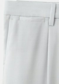 Pantalon gris clair ajusté montrant la taille, les passants de ceinture et une poche latérale avec un tissu finement texturé.