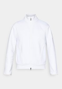 Hvit jakke med glidelås og h�øy krage, med teksturert stoff, flate sømmer og en liten logo på venstre erme. Fungerer med sidelommer.