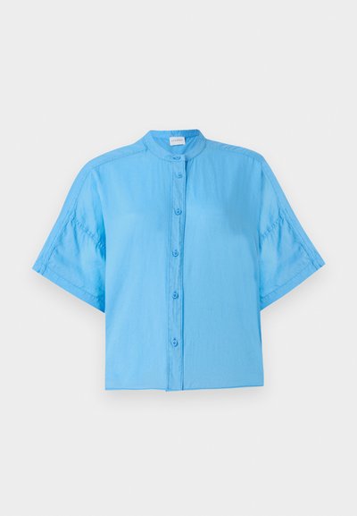 Camisa azul-claro de manga curta com colarinho mandarim, apresentando um corte descontraído e um brilho subtil no tecido. Bainha arredondada.