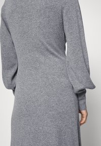 Šedé pletené šaty s texturou, dlouhými objemnými rukávy a přiléhavým střihem, které se vyznačují jemným povrchem látky.