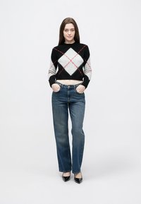 Čierny, sivý a biely krátky sveter so vzorom červeného diamantu; skombinovaný s modrými riflemi s vysokým pásom a čiernymi topánkami so špicatou špičkou.