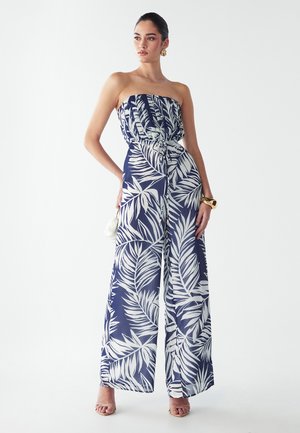 Jumpsuit sans manches de couleur marine avec imprimé de feuilles tropicales blanches, taille cintrée, design à jambes larges et tissu doux et léger. Silhouette élégante.