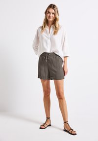 Lehká, volná bílá košile na knoflíky spárovaná se šedými kraťasy po kolena s elastickým páskem a šňůrkou. Černé sandály na pásku.