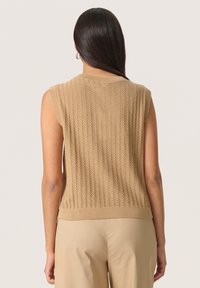 Stickad ärmlös topp i ljusbeige med texturerat mönster och ribbad kant. Har en figursydd siluett och en slät yta.