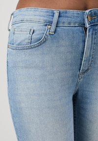 Light blue denim jeans featuring a fitted design, front pockets, and visible stitching details. Fabric displays a faded texture.