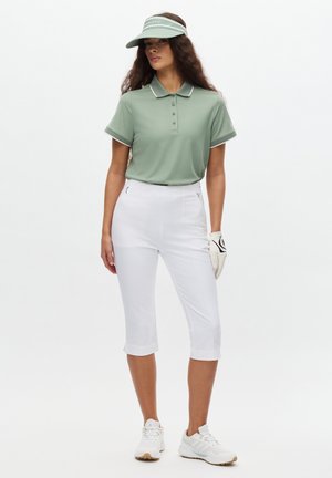 Polo de color verde claro con cuello y botones, combinado con pantalones blancos recortados. Los accesorios incluyen una visera y un guante de golf blanco.