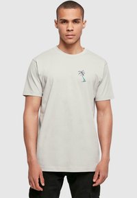 Light grey cotton t-shirt featuring a small embroidered palm tree design on the left chest area. Short sleeves, crew neckline.