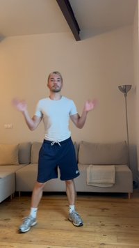 Homme en t-shirt blanc et short bleu marine qui fait de l'exercice à l'intérieur près d'un canapé beige et d'une lampe sur pied sur un sol en bois.