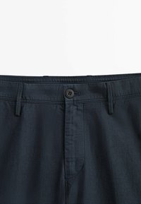 Tummansininen, teksturoitu kangashousu, jossa on nappikiinnitys, vyölenkit ja yksi etutasku. Suunnittelussa on vaalea kudottu kuvio.