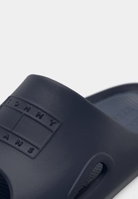 Mørkeblå glidisandal laget av strukturert syntetisk materiale, med et fremtredende preget logo og utskjæringer for ventilasjon.