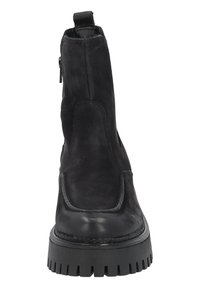 Botín negro de tobillo con acabado de ante, punta redondeada y suela de goma gruesa y texturizada. Cuenta con un cierre lateral y acentos de costura.