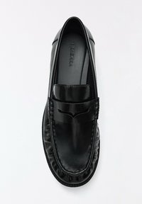 Mocassin en cuir noir avec couture mocassin et détail d'une bride penny, vu de dessus sur fond blanc.
