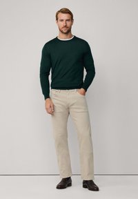 Maglione a maniche lunghe verde scuro con colletto bianco, abbinato a pantaloni dritti beige chiaro e scarpe scure. Design semplice e moderno.
