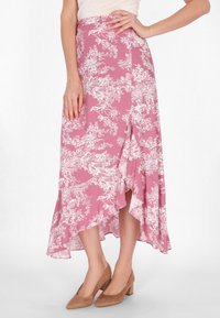 Fustă florale roz cu modele botanice albe, având un tiv volanat și o deschidere pe lateral. Asortată cu pantofi cu toc bloc maro.