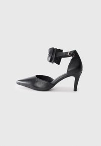 Black leather high-heeled shoe with a pointed toe, ankle strap featuring a bow accent, and a sleek, smooth texture.