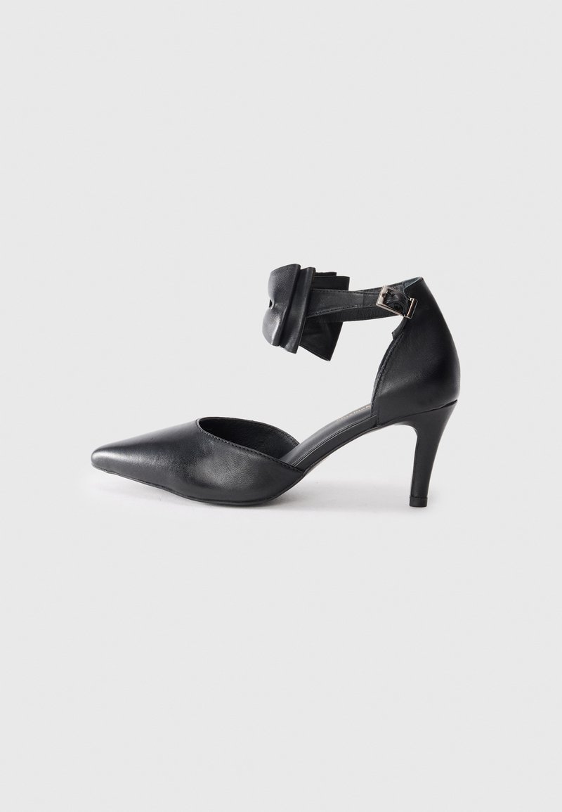 Black leather high-heeled shoe with a pointed toe, ankle strap featuring a bow accent, and a sleek, smooth texture.
