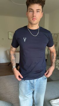 Camiseta de manga corta en azul marino, hecha de algodón, con un pequeño emblema de un ciervo blanco en el pecho y una textura suave.