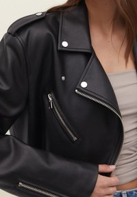 Musta nahkainen moottoripyöräjacketti, jossa on hopeiset yksityiskohdat, kuten vetoketjut ja niitit. Rakenne hartioissa ja slim fit -muotoilu.