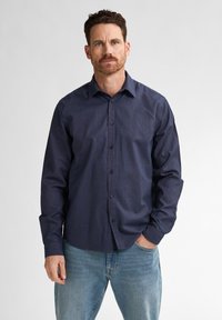 Miestens tamsiai mėlyna marškinė su mygtukais, pagaminta iš lengvos medžiagos. Turi ilgomis rankovėmis, su mygtukais ant riešo ir klasikiniu apykaklės dizainu. Dėvimi su šviesiomis džinsinėmis kelnėmis.