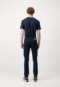 Navy t-shirt, blue jeans with leather patch at the back, and sneakers. Features a fitted design and standard straight leg cut.