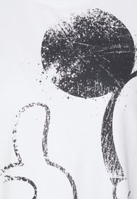 Bílý tričko s velkým černým kruhovým potiskem a abstraktním liniovým designem. Textura je hladká, vyrobené z měkké bavlny.