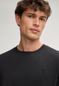 Czarny sweter crew-neck wykonany z miękkiego materiału, z delikatnie haftowanym logo na klatce piersiowej oraz prążkowanym dekoltem i mankietami.