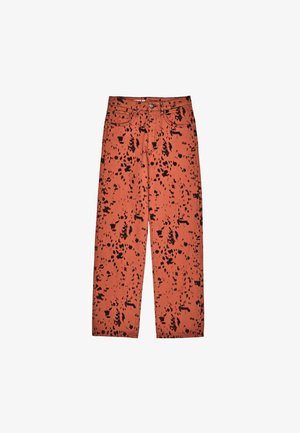 Orange denim jeans featuring a splattered black pattern, five pockets, and a straight leg design. Standard button and zipper closure.