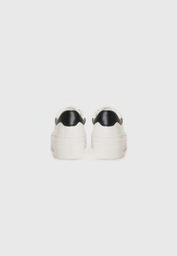 Vita sneakers med en strukturerad sula och scallop-mönstrade svarta detaljer vid hälen. Slät ovandel, rund tå, minimalistisk design.