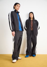 Svart treningsjakker med hvite striper, svarte bukser med sidelister og fargerike topper. Modellene har på seg blå og hvite joggesko.