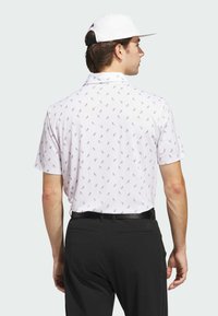 White short-sleeve polo with a geometric pattern, paired with black trousers. The polo features a subtle texture and a classic collar.