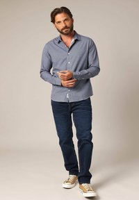 Heren blauwe en witte gestreepte overhemd met lange mouwen, gecombineerd met navy jeans en tan sneakers. Van katoen, met kraagontwerp.