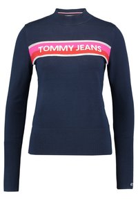Mörkblå långärmad tröja med ribbade mudd och fåll, hög hals, samt ett randigt mönster i rosa, rött och vitt med "TOMMY JEANS" över bröstet.