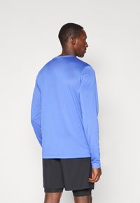 Langærmet atletisk skjorte i blå, lavet af let og glat stof. Har en rund halsudskæring og kontrasterende sorte shorts.
