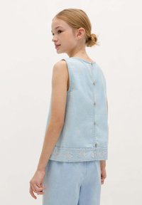 Lichtblauwe denim mouwloze top met een rechte snit, geborduurde onderzoom en kleine knopen op de achterkant. Vlakke textuur, casual ontwerp.