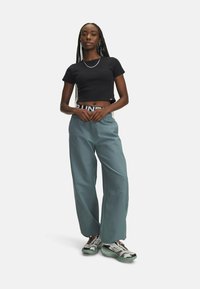 Black cropped t-shirt, loose teal pants with an elastic waistband and side pockets, paired with multi-colored sneakers featuring a textured sole.