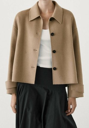 Beige wool-blend cropped jacket with a notched collar, six-button closure, and oversized cuffs, paired with a white top and black skirt.