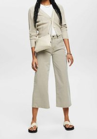 Cardigan beige côtelé, t-shirt blanc, jean large couleur vert clair et sac beige. Sandales noires avec brides croisées. Ensemble simple et décontracté.