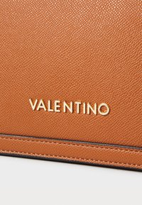 Brahno usnjeno torbico z zlatim logotipom "VALENTINO". Očitna podrobnost šivanja ob robovih in gladek zaključek.